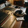Composición de estudio con auriculares profesionales, mesa de mezclas analógica y notas sobre fondo oscuro.