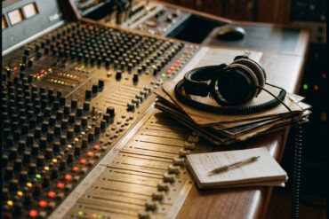 Composición de estudio con auriculares profesionales, mesa de mezclas analógica y notas sobre fondo oscuro.