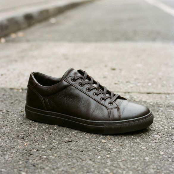 Zapatillas bajas de cuero oscuro sobre el asfalto en plano detalle editorial.