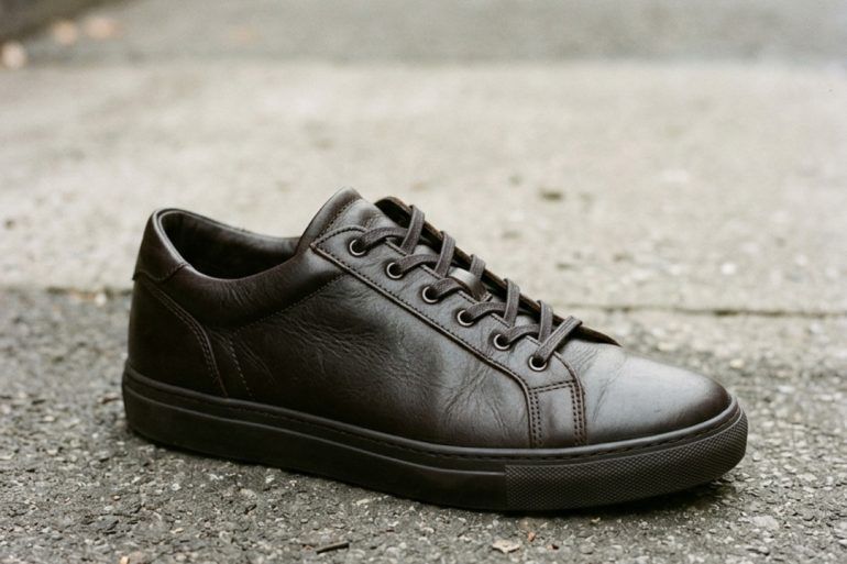 Zapatillas bajas de cuero oscuro sobre el asfalto en plano detalle editorial.