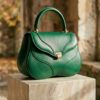 Bolso de mano de piel verde esmeralda con diseño orgánico sobre una superficie neutra elegante de otoño