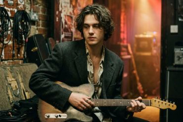 Guitarrista de estilo indie afinando su guitarra eléctrica entre bastidores con luz cálida y estética cinematográfica.