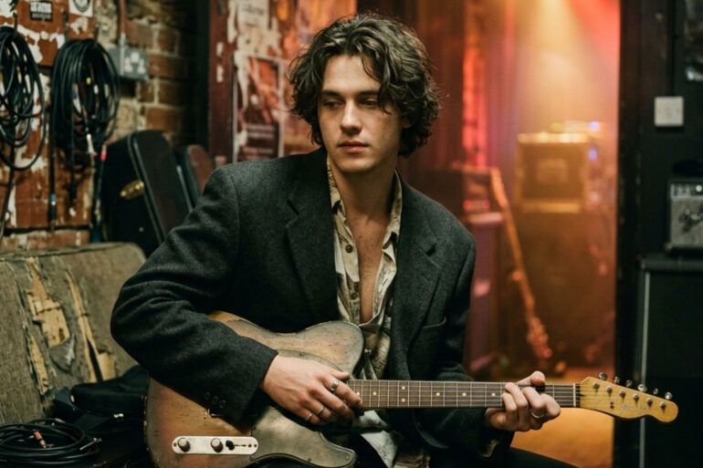 Guitarrista de estilo indie afinando su guitarra eléctrica entre bastidores con luz cálida y estética cinematográfica.
