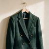 Chaqueta de corte preppy estructurada en lana sobre un perchero de madera con luz natural de otoño.