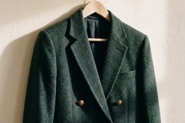 Chaqueta de corte preppy estructurada en lana sobre un perchero de madera con luz natural de otoño.