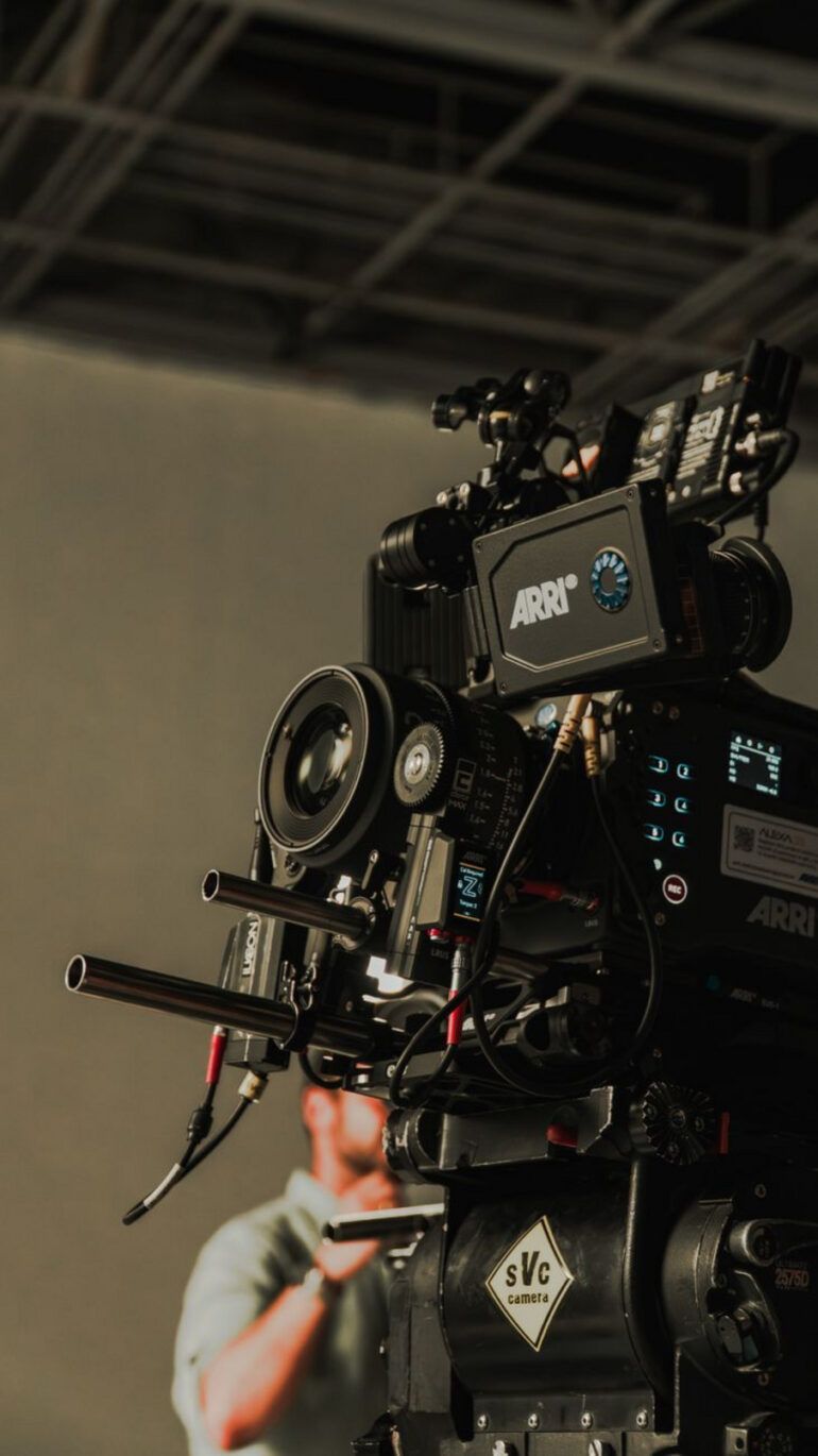 Cámara de cine profesional en un set de rodaje iluminado con sombras dramáticas y atmósfera cinematográfica.