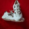 Zapatillas clásicas de piel blanca sobre suelo de galería de arte con luz natural lateral