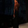Modelos desfilando con prendas de sastrería y vestidos fluidos sobre una pasarela de moda con iluminación tenue
