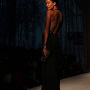 Modelos desfilando con prendas de sastrería y vestidos fluidos sobre una pasarela de moda con iluminación tenue