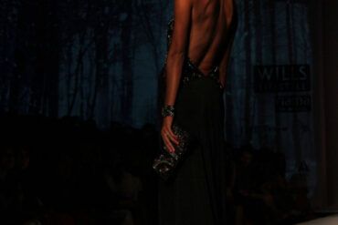 Modelos desfilando con prendas de sastrería y vestidos fluidos sobre una pasarela de moda con iluminación tenue