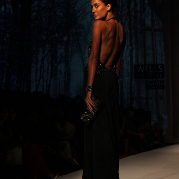 Modelos desfilando con prendas de sastrería y vestidos fluidos sobre una pasarela de moda con iluminación tenue