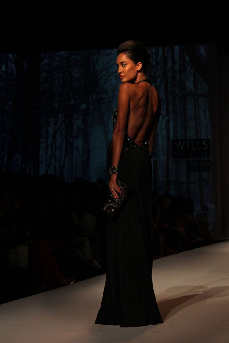 Modelos desfilando con prendas de sastrería y vestidos fluidos sobre una pasarela de moda con iluminación tenue