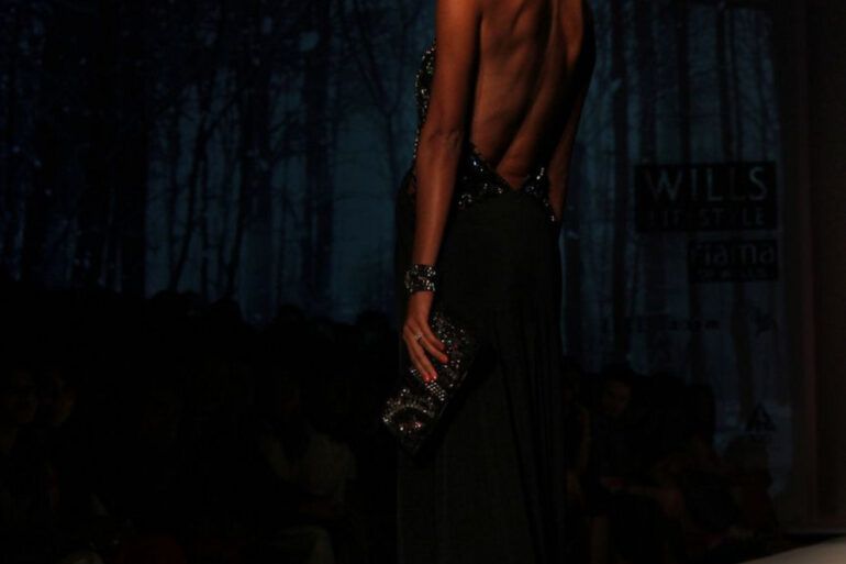 Modelos desfilando con prendas de sastrería y vestidos fluidos sobre una pasarela de moda con iluminación tenue
