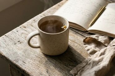 Mesa de madera con una taza de cerámica, libreta de notas y servilleta de lino bajo luz natural matinal