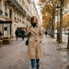 Mujer vestida con gabardina beige clásica y vaqueros rectos paseando por la ciudad