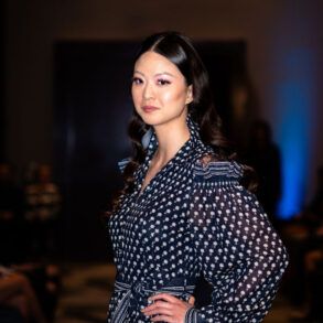 Modelo desfilando en pasarela con prenda de sastrería oscura de corte afilado e iluminación editorial.