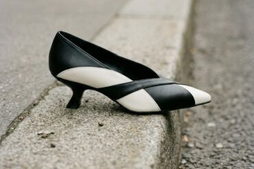 Primer plano de calzado de tacón bajo kitten heel sobre bordillo de cemento urbano con luz natural.