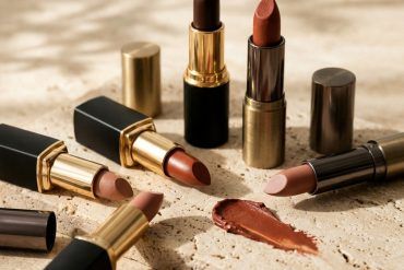 Tres barras de labiales marrones en tonos tostados y chocolate colocadas sobre una bandeja minimalista con luz natural.