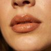 Primer plano de labios carnosos con perfilado cálido y acabado brillante de aceite labial con luz natural.