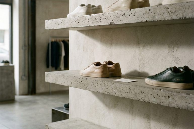 Zapatillas urbanas ordenadas en baldas minimalistas de hormigón con iluminación natural de estudio.