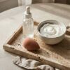 Frasco de sérum de cuidado facial sobre bandeja de mármol con toalla de algodón y luz suave de mañana