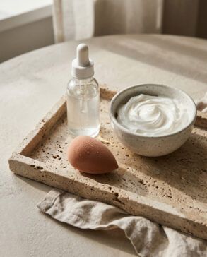 Frasco de sérum de cuidado facial sobre bandeja de mármol con toalla de algodón y luz suave de mañana
