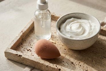 Frasco de sérum de cuidado facial sobre bandeja de mármol con toalla de algodón y luz suave de mañana