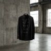 Chaqueta negra de inspiración militar con detalles metálicos sobre fondo neutro en un entorno urbano de estilo editorial