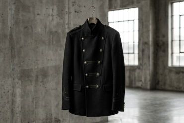 Chaqueta negra de inspiración militar con detalles metálicos sobre fondo neutro en un entorno urbano de estilo editorial