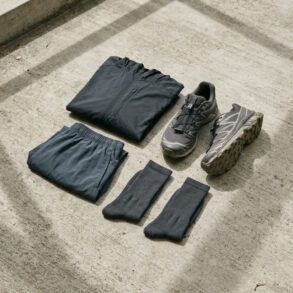 Detalle de zapatillas de running y prendas técnicas de diseño minimalista sobre suelo de hormigón con luz natural.