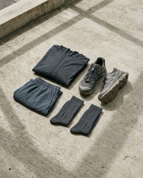 Detalle de zapatillas de running y prendas técnicas de diseño minimalista sobre suelo de hormigón con luz natural.