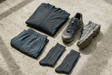 Detalle de zapatillas de running y prendas técnicas de diseño minimalista sobre suelo de hormigón con luz natural.