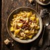 Cazuela rústica de pasta mista con patatas, panceta y queso derretido sobre mesa de madera