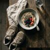 Mesa de madera con desayuno saludable de avena, frutos secos y zapatillas de deporte preparadas para entrenar.