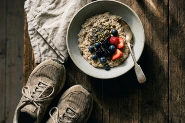 Mesa de madera con desayuno saludable de avena, frutos secos y zapatillas de deporte preparadas para entrenar.