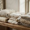 Detalle de prendas de ropa de lino y lana dobladas con cuidado en un estante de madera natural con luz suave.