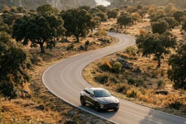 Coche elegante en una carretera secundaria atravesando un paisaje de dehesa dorada y colinas al atardecer de otoño