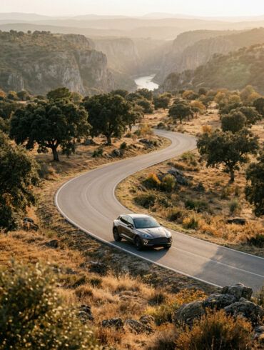 Coche elegante en una carretera secundaria atravesando un paisaje de dehesa dorada y colinas al atardecer de otoño
