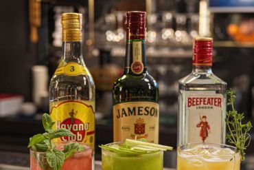 Barra elegante de coctelería con copas de cristal y botellas de destilados bajo luz cálida editorial.