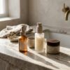 Frascos minimalistas de cosmética y texturas hidratantes sobre un tocador elegante con luz natural matutina.
