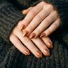 Manicura con uñas efecto cobre brillante apoyada sobre tejido de punto oscuro.