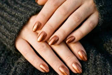 Manicura con uñas efecto cobre brillante apoyada sobre tejido de punto oscuro.