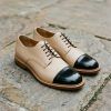 Primer plano cenital de zapatos bicolor de piel sobre suelo urbano limpio con luz natural de otoño